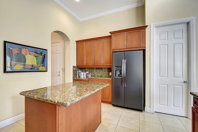 kitchen featuring light tile patterned flooring, dark stone counters, stainless steel refrigerator with ice dispenser, ornamental molding, and a kitchen island