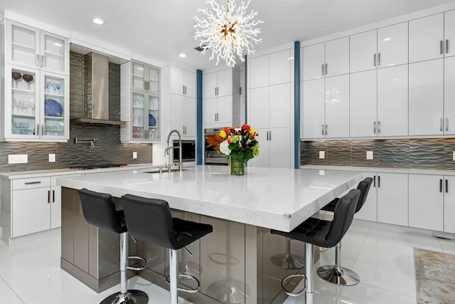 kitchen featuring sink, a breakfast bar, a kitchen island with sink, white cabinets, and wall chimney exhaust hood