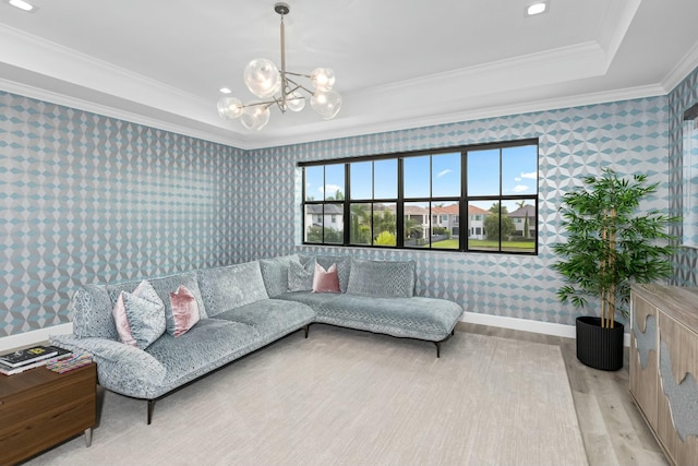 living room with an inviting chandelier, ornamental molding, a raised ceiling, and light wood-type flooring