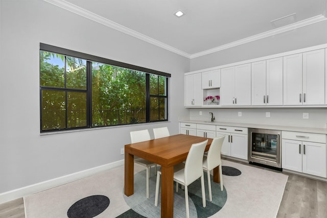 dining room featuring crown molding, sink, beverage cooler, and light hardwood / wood-style floors