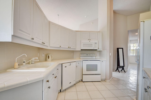 kitchen with tile counters, light tile patterned flooring, lofted ceiling, white appliances, and white cabinets