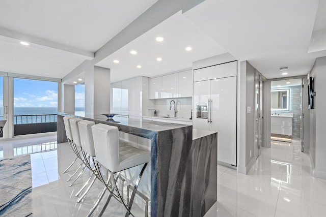 kitchen featuring a kitchen breakfast bar, dark stone counters, stainless steel built in refrigerator, a water view, and white cabinets