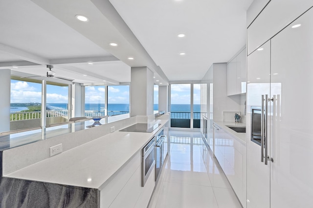 kitchen featuring a water view, light tile patterned floors, black electric cooktop, a large island, and white cabinetry