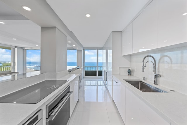 kitchen with white cabinetry, sink, light tile patterned floors, black electric stovetop, and a water view