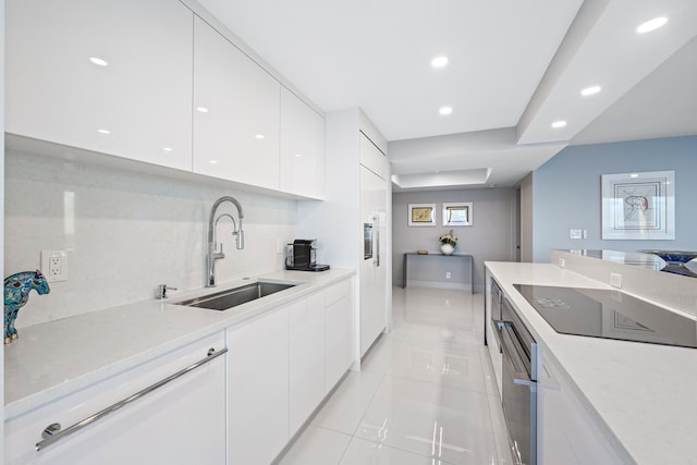 kitchen featuring stainless steel oven, black electric cooktop, sink, light tile patterned floors, and white cabinetry