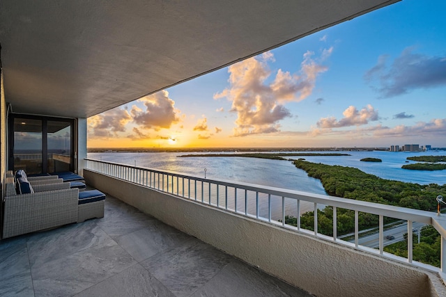 balcony at dusk featuring a water view