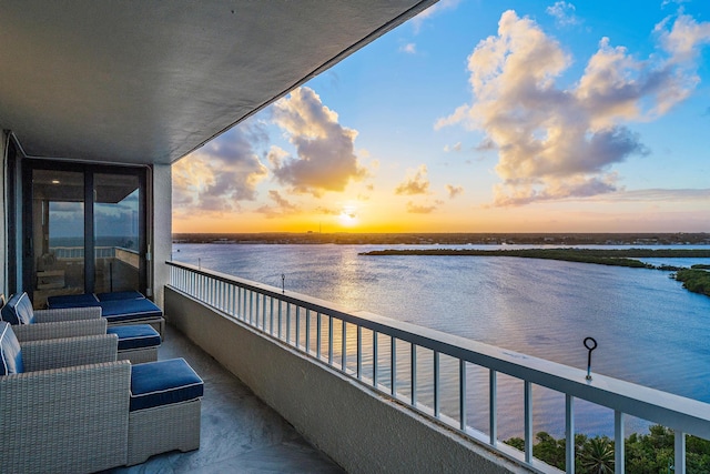 balcony at dusk featuring a water view