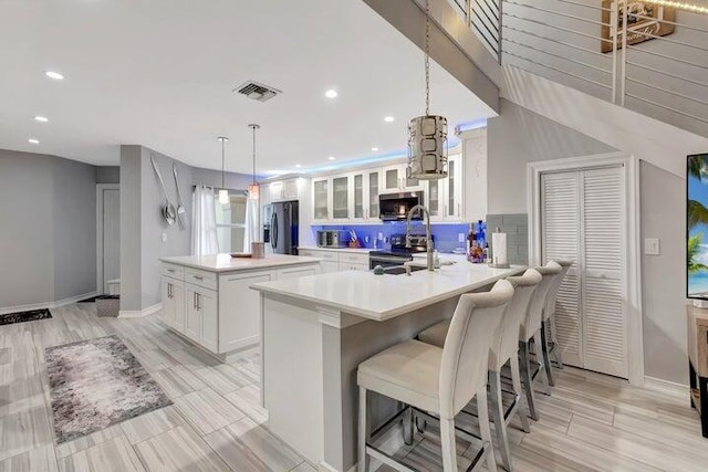 kitchen featuring a center island with sink, white cabinets, hanging light fixtures, and appliances with stainless steel finishes