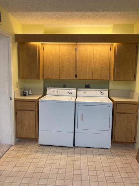 clothes washing area with washer and dryer, light tile patterned floors, cabinets, and a textured ceiling