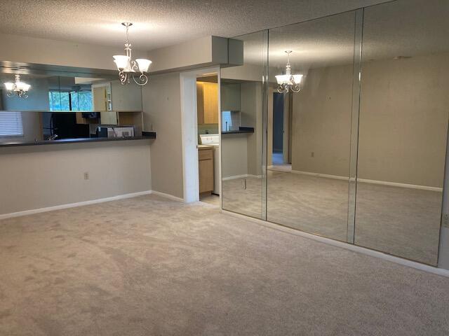 kitchen featuring a textured ceiling, light carpet, and an inviting chandelier