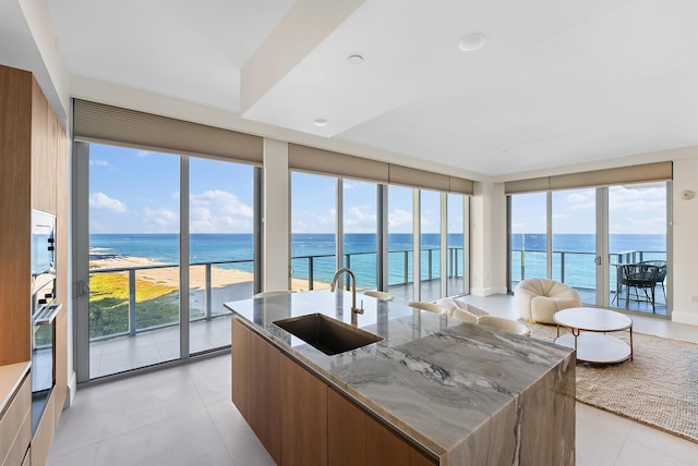 kitchen featuring sink, a water view, oven, light stone countertops, and a center island with sink