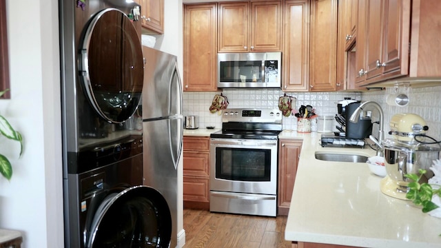 kitchen featuring tasteful backsplash, stainless steel appliances, sink, wood-type flooring, and stacked washer and dryer