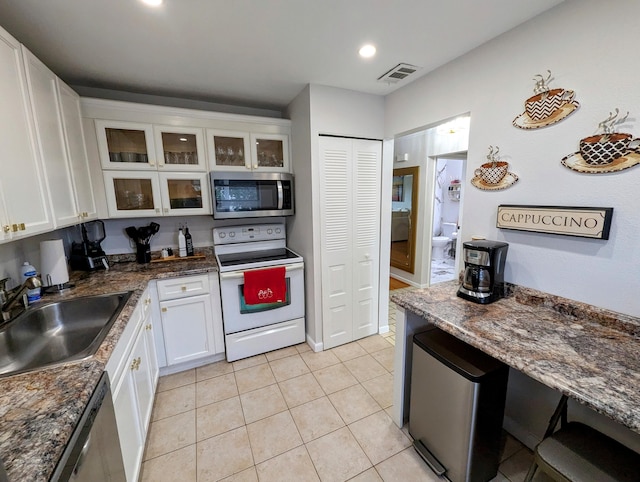 kitchen featuring dark stone counters, sink, light tile patterned floors, white cabinetry, and stainless steel appliances