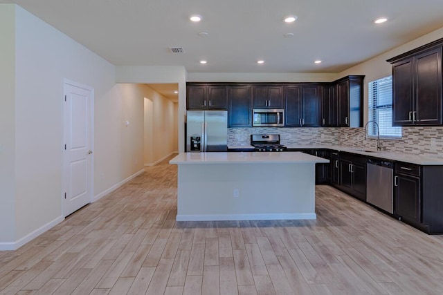 kitchen with appliances with stainless steel finishes, light wood-type flooring, a sink, and decorative backsplash