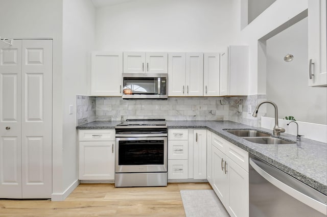 kitchen featuring sink, light hardwood / wood-style flooring, backsplash, white cabinets, and appliances with stainless steel finishes