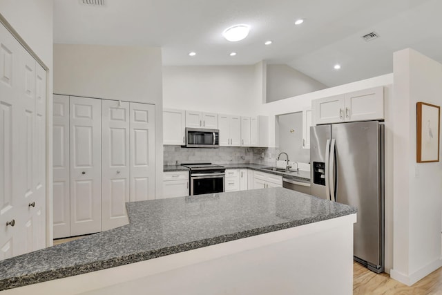 kitchen with dark stone countertops, white cabinets, stainless steel appliances, and light hardwood / wood-style floors