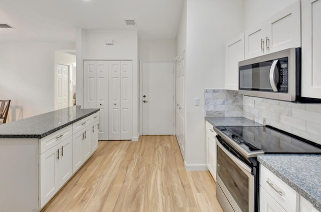 kitchen featuring appliances with stainless steel finishes, light wood-type flooring, backsplash, dark stone counters, and white cabinets