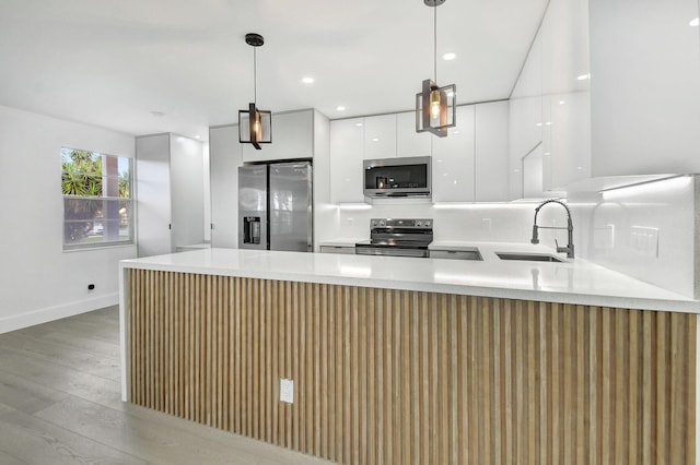 kitchen featuring appliances with stainless steel finishes, sink, decorative light fixtures, light hardwood / wood-style flooring, and white cabinets