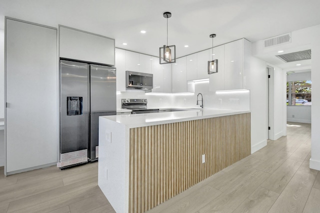 kitchen featuring white cabinets, hanging light fixtures, light hardwood / wood-style flooring, appliances with stainless steel finishes, and kitchen peninsula