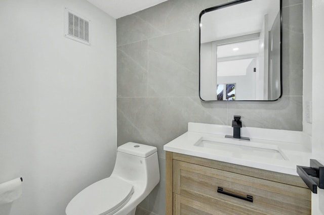 bathroom featuring vanity, toilet, and tile walls