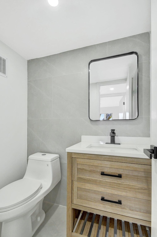 bathroom featuring tile patterned flooring, vanity, toilet, and tile walls