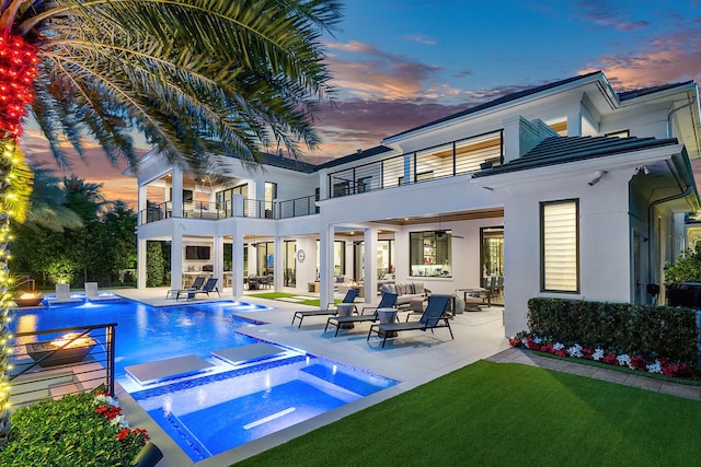 back house at dusk featuring a patio area, ceiling fan, a balcony, and a pool with hot tub