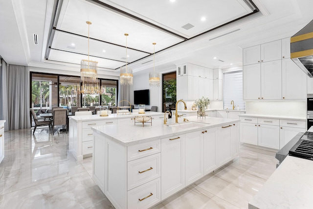 kitchen with light stone countertops, sink, pendant lighting, a center island with sink, and white cabinetry