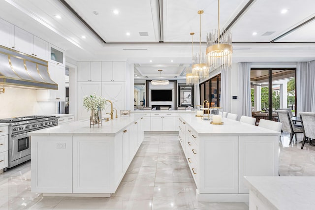 kitchen featuring light stone countertops, a raised ceiling, a spacious island, stainless steel stove, and hanging light fixtures