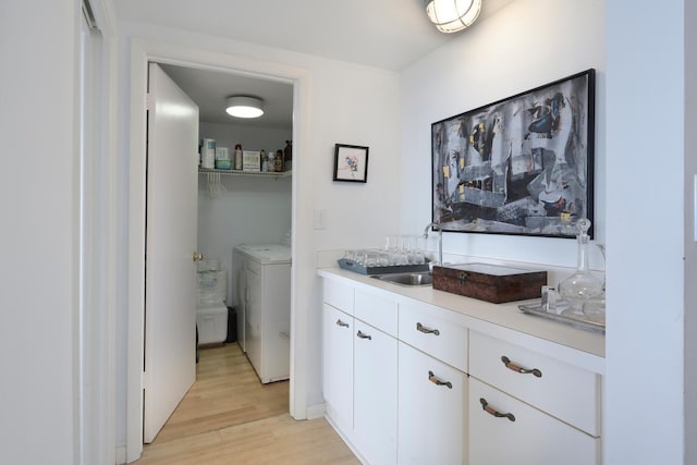 clothes washing area with washer and dryer, sink, and light hardwood / wood-style flooring