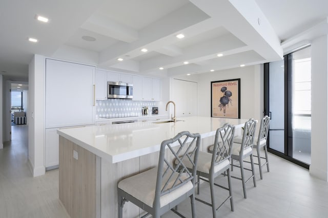 kitchen with a kitchen breakfast bar, sink, beam ceiling, white cabinetry, and a large island