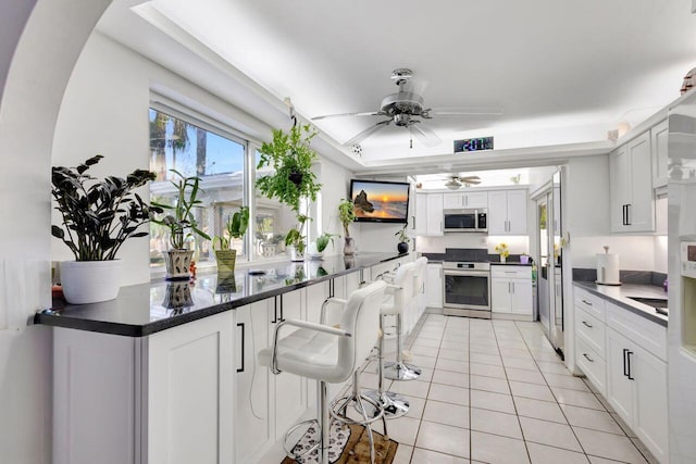 kitchen with ceiling fan, light tile patterned flooring, a breakfast bar, white cabinets, and appliances with stainless steel finishes