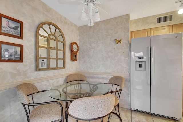 dining space featuring visible vents, a wainscoted wall, a ceiling fan, wallpapered walls, and light tile patterned floors