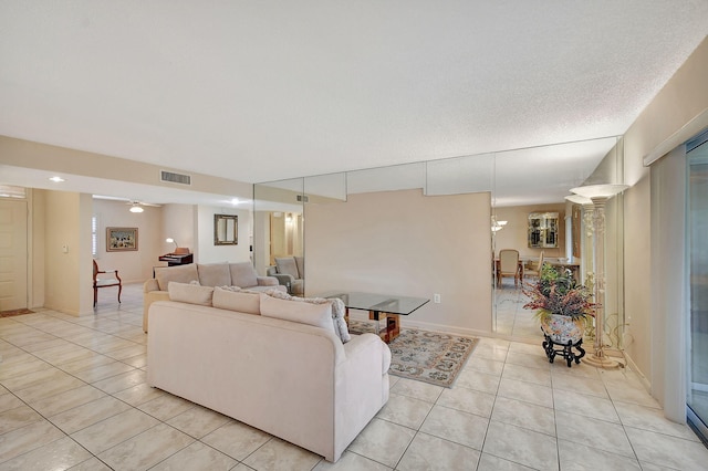 living area featuring light tile patterned flooring, visible vents, a textured ceiling, and ceiling fan