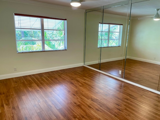 unfurnished bedroom featuring wood-type flooring, a closet, multiple windows, and crown molding