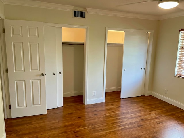 unfurnished bedroom with dark hardwood / wood-style floors, multiple closets, and crown molding