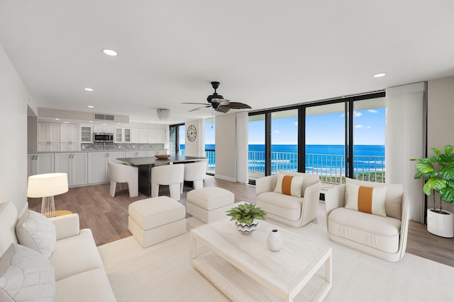 living room with ceiling fan, expansive windows, a water view, and light hardwood / wood-style flooring