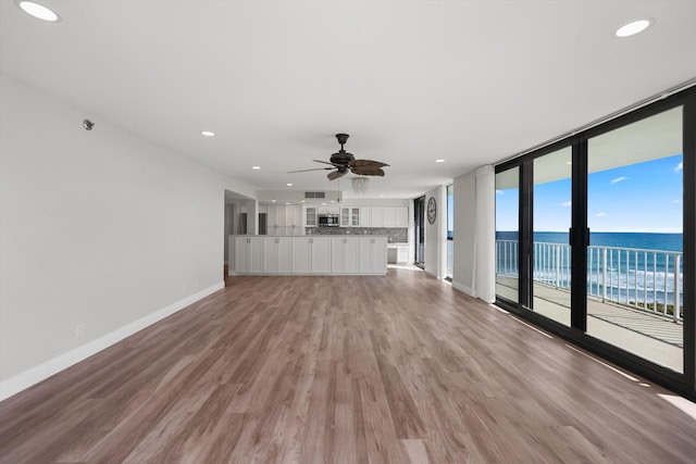 unfurnished living room with a water view, ceiling fan, and light hardwood / wood-style floors