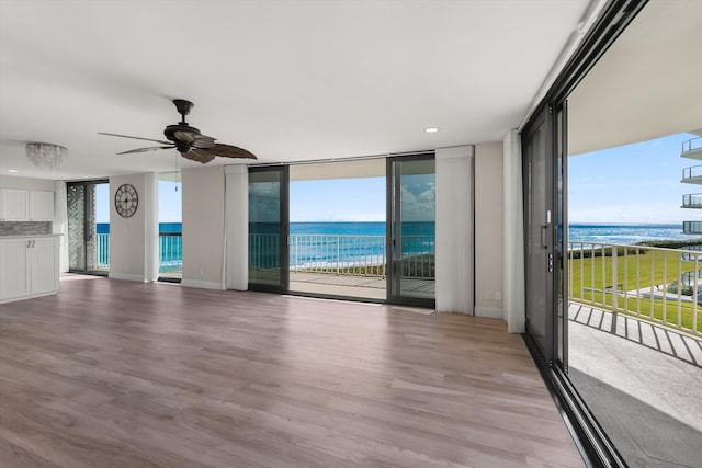 unfurnished living room featuring expansive windows, light hardwood / wood-style floors, a wealth of natural light, and a water view