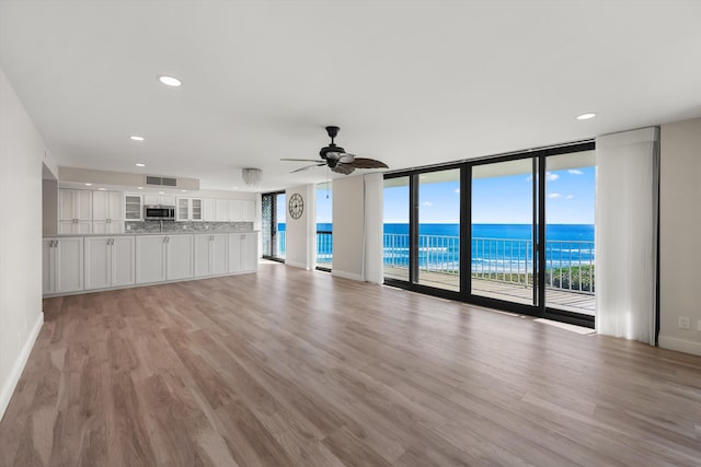 unfurnished living room featuring expansive windows, light wood-type flooring, a water view, and ceiling fan