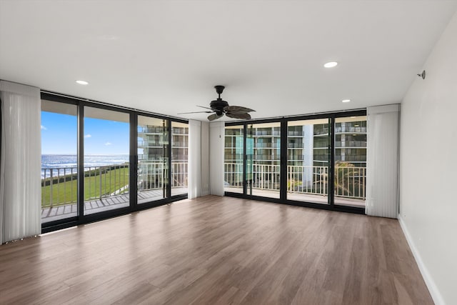 unfurnished room with expansive windows, ceiling fan, a water view, and wood-type flooring