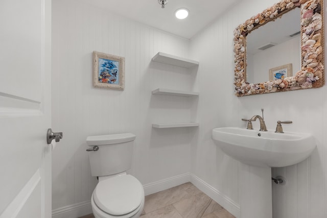 bathroom with toilet, sink, and wooden walls