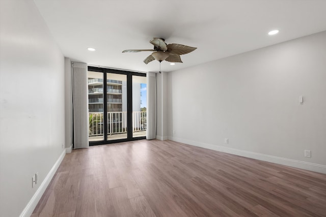 empty room featuring hardwood / wood-style flooring, ceiling fan, and a wall of windows