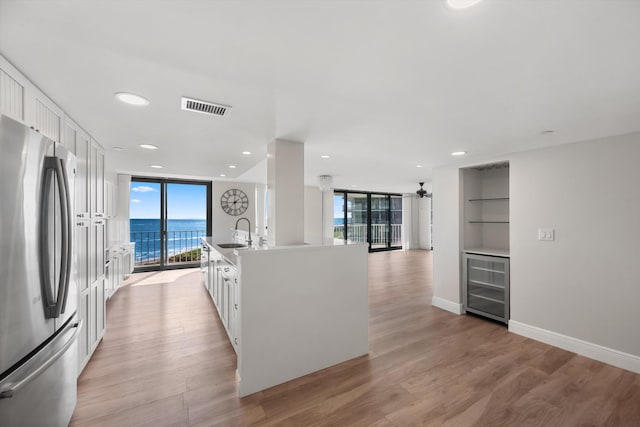 kitchen with a water view, light hardwood / wood-style flooring, stainless steel fridge, an island with sink, and white cabinetry