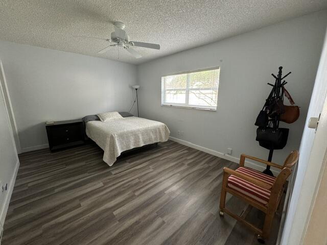 bedroom with a textured ceiling, ceiling fan, and dark wood-type flooring