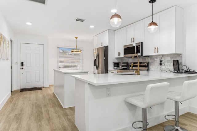 kitchen featuring kitchen peninsula, a breakfast bar, stainless steel appliances, light hardwood / wood-style flooring, and white cabinets