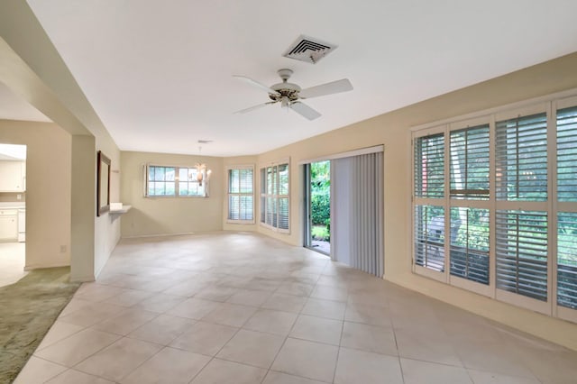 tiled spare room featuring ceiling fan with notable chandelier