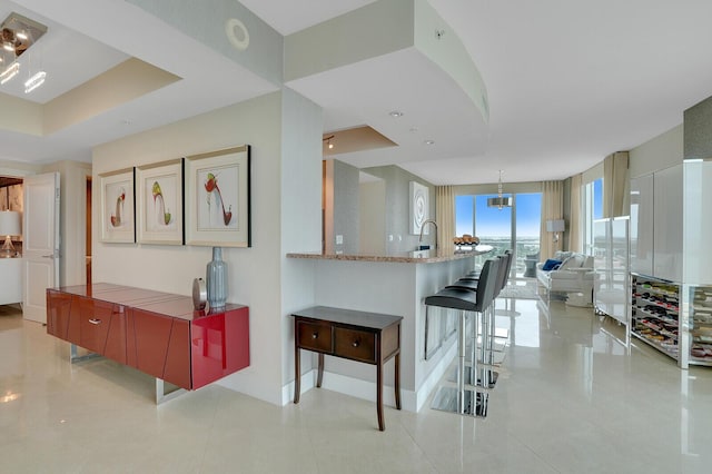 kitchen featuring kitchen peninsula, a kitchen breakfast bar, light stone counters, a raised ceiling, and a wall of windows