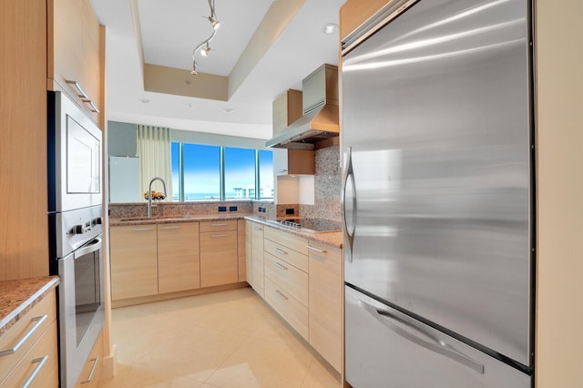 kitchen featuring light stone countertops, light brown cabinetry, decorative backsplash, stainless steel appliances, and sink