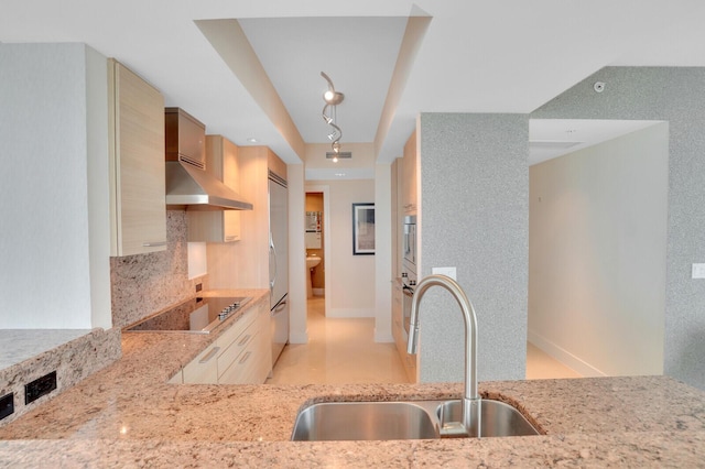 kitchen with wall chimney range hood, sink, light stone countertops, tasteful backsplash, and electric stovetop