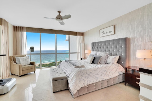 bedroom with ceiling fan, a water view, and a wall of windows